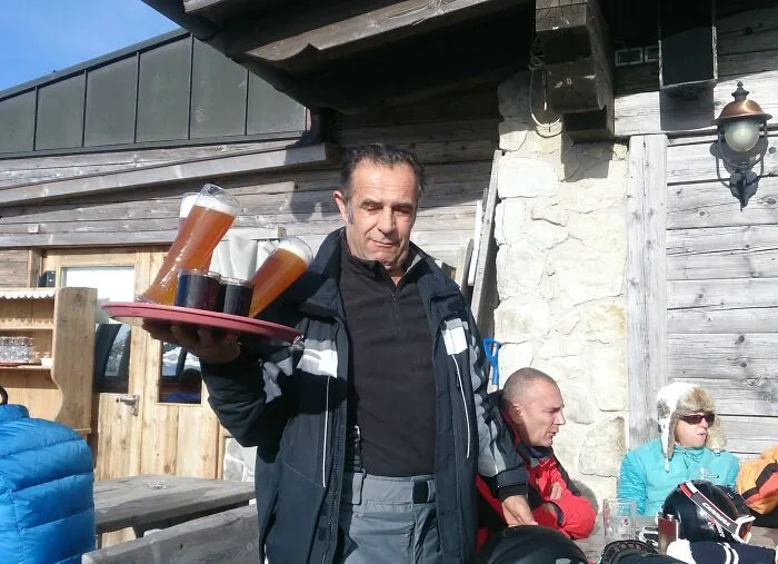 Hombre llevando varias cervezas en un bar al aire libre justo antes de que ocurra un accidente divertido.