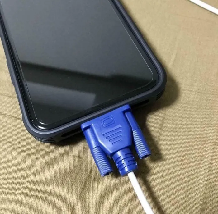 Smartphone with an incompatible blue VGA cable plugged in, illustrating common mistakes in handling electronics and soldering issues.