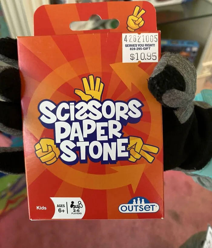 Packaging of a game called Scissors Paper Stone held by gloved hands, showcasing a nonsensical item that actually exists.