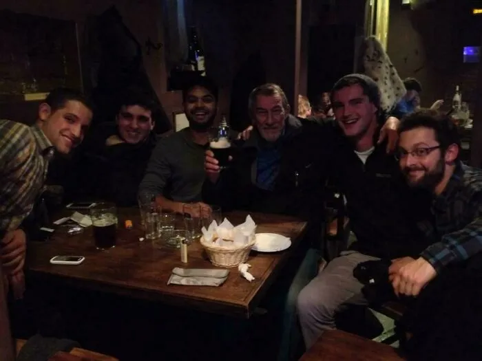 Group of men in a pub laughing and posing with a man resembling a celebrity in a casual social setting.