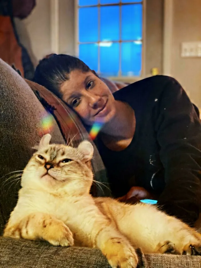 Woman relaxing on a couch with a cat that looks unusual, highlighting cats as possible mysterious aliens.