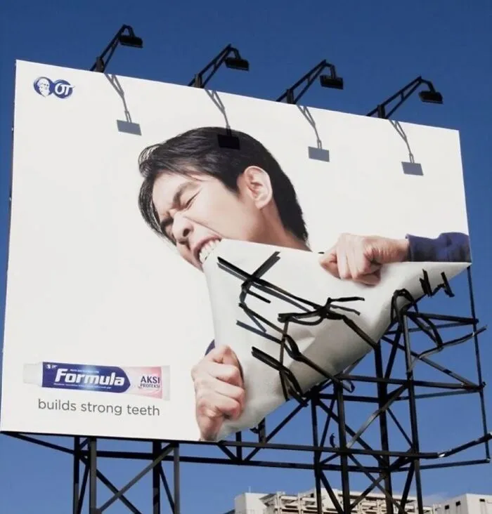Valla publicitaria divertida y creativa de pasta dental con hombre mordiendo un objeto, ejemplo de carteles divertidos y brillantes.