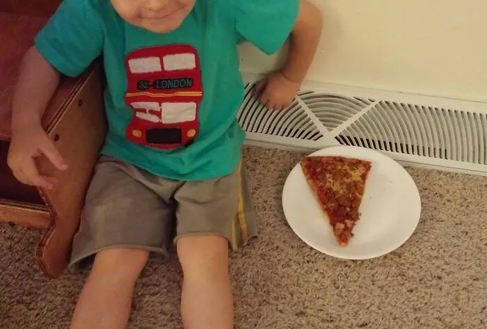 Child sitting on carpet next to a slice of pizza on a plate, showcasing creativity and invention in a home setting.