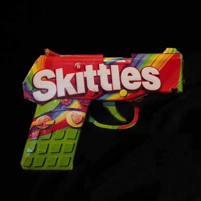 Sculpture of a gun made from Skittles packaging, showcasing the artist turning waste into witty commentary on modern life.