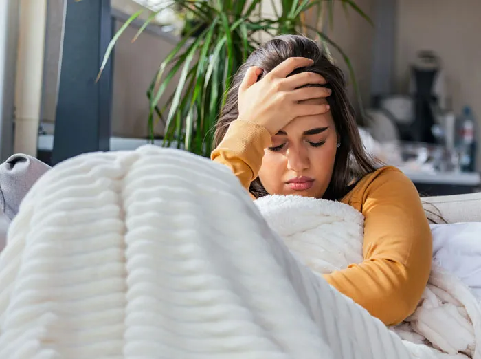 Mujer con expresión preocupada, recostada en sofá con manta blanca, simbolizando teléfonos que revelan verdades ocultas.
