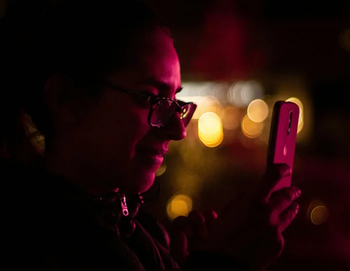 Persona con gafas usando un teléfono móvil de noche, mostrando cómo los teléfonos ayudan a descubrir verdades ocultas.