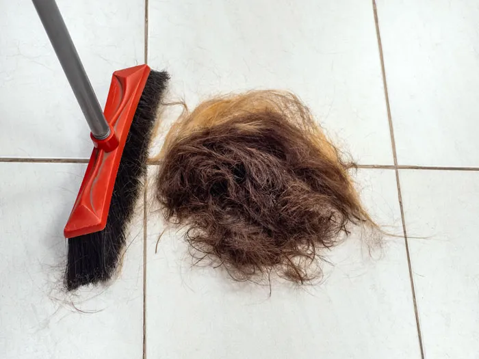 Broom beside a large clump of hair on white tile floor, illustrating unexpected things men didn’t know about women.