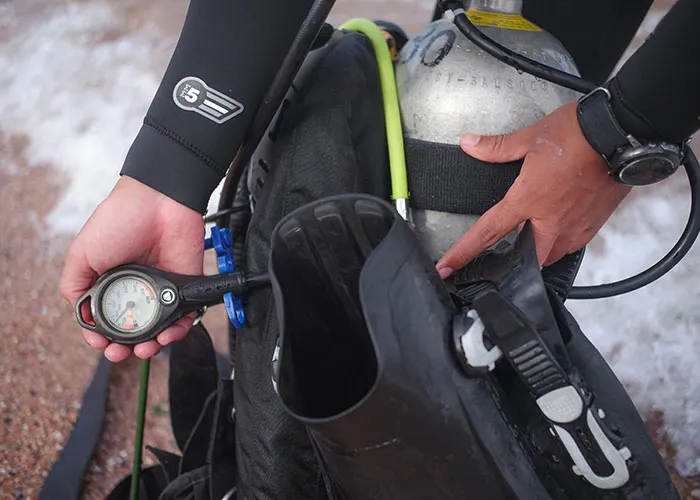 Close-up of a diver’s hands checking scuba gear and pressure gauge, ready for a terrifying true story underwater experience.