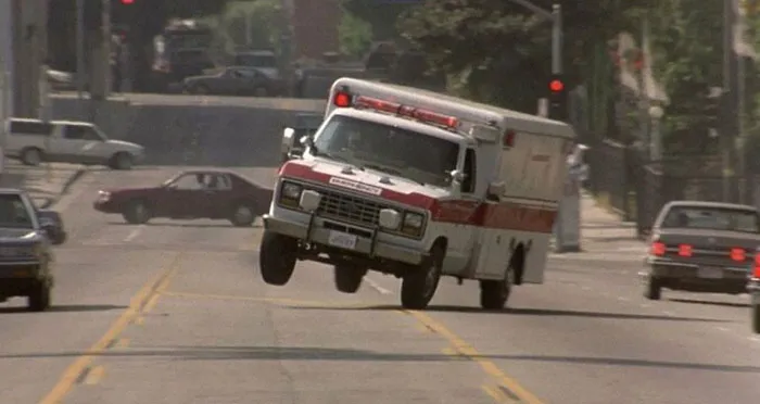 Ambulance driving quickly with front wheels lifted off the road, showcasing EMT and paramedic emergency response action.