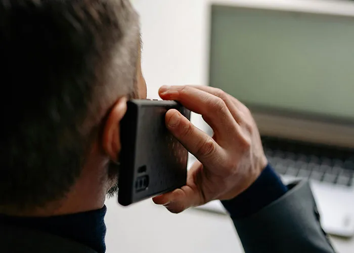 Man holding a phone to his ear while sitting near a laptop, illustrating a moment in criminal fails caught on camera.