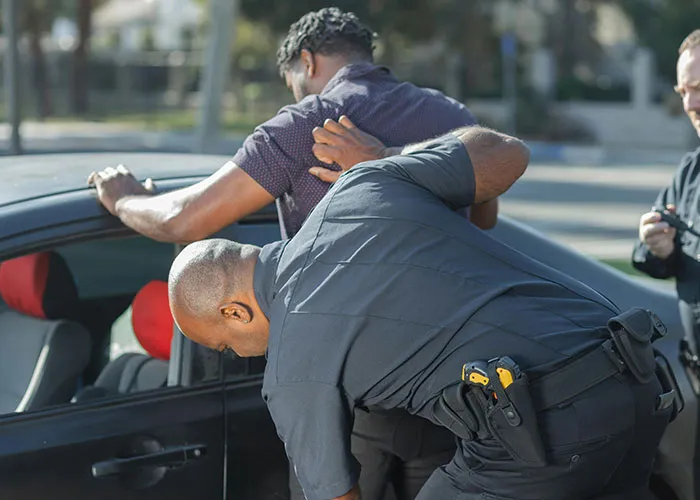 Police officer handcuffing a man in a criminal fail during a traffic stop on a sunny day.