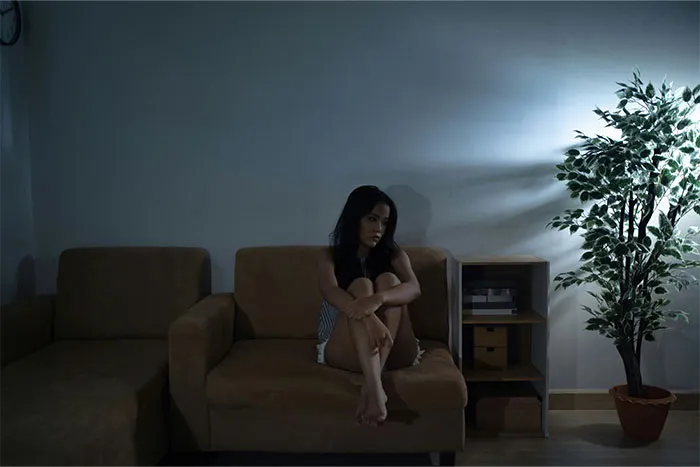 Woman sitting alone on couch in dark room with mysterious lighting, illustrating bizarre and paranormal experiences concept