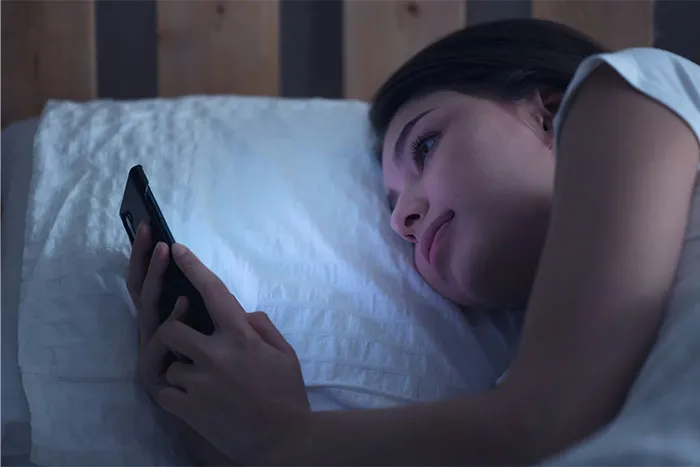 Young woman lying in bed at night, looking at phone screen, experiencing a bizarre and paranormal moment.