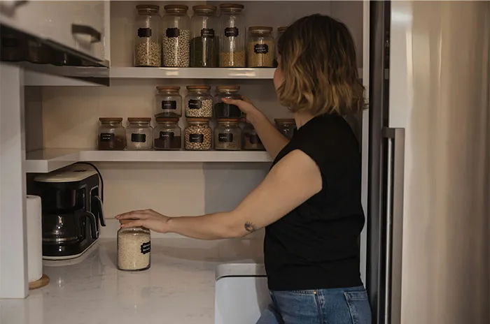 Woman organizing jars on kitchen shelves, surrounded by various containers, representing bizarre and paranormal experiences.
