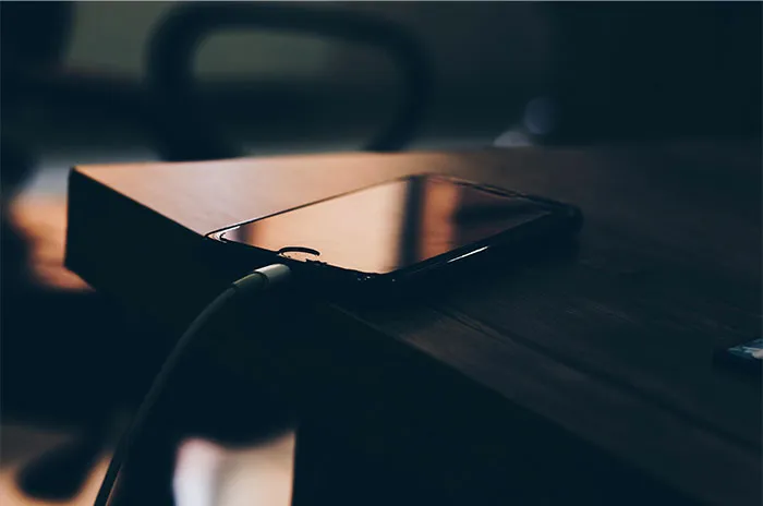 Smartphone on a wooden table charging in low light, symbolizing bizarre and paranormal experiences in a modern setting.