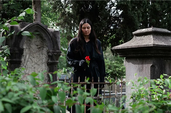 Woman in black holding a red rose at a graveyard surrounded by eerie trees, evoking paranormal experiences and mystery.