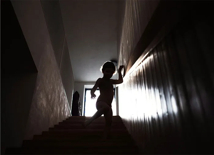 Silhouetted child descending dimly lit stairs, evoking bizarre and paranormal experiences in a mysterious indoor setting.
