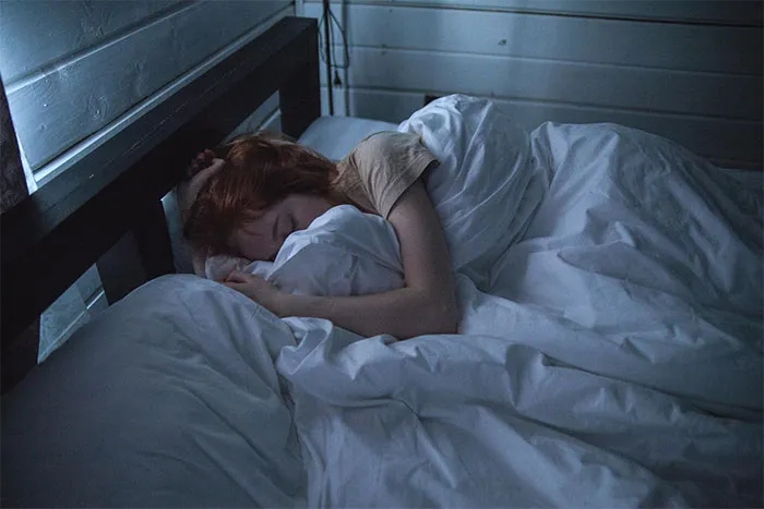 Person sleeping in a dimly lit bedroom, wrapped in white sheets, suggesting a setting for paranormal experiences.