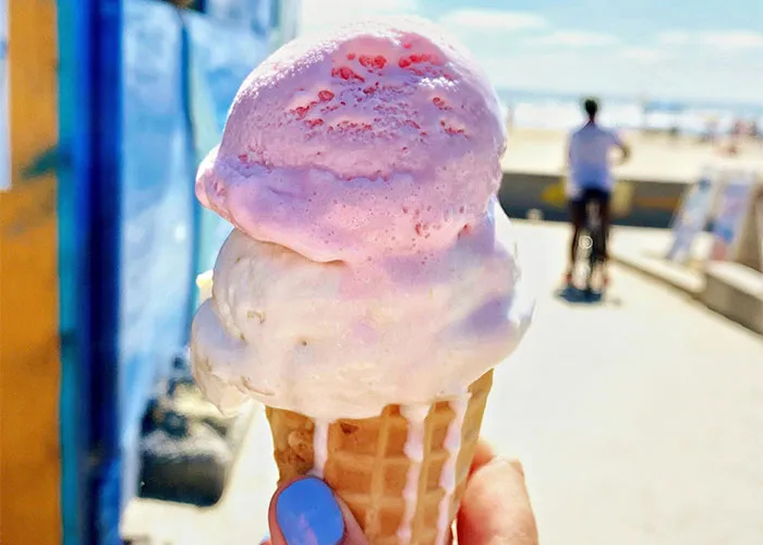 Close-up of melting ice cream cone held outdoors with blurred person biking in the background, showcasing unique body quirks.
