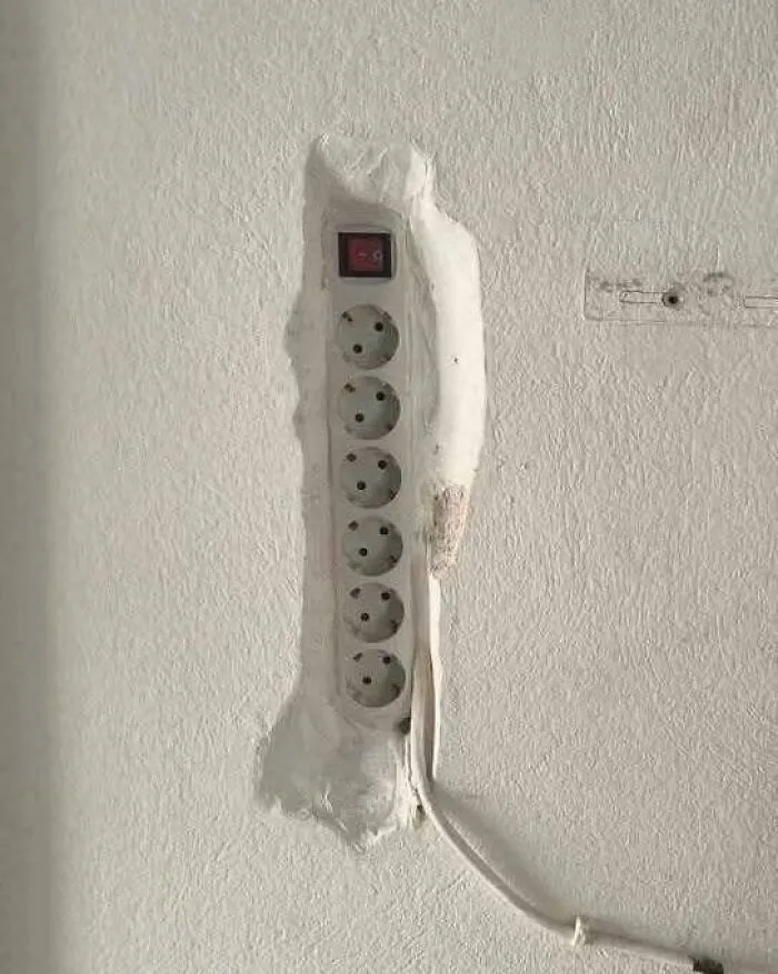 Enchufe múltiple mal instalado en pared, mostrando un claro error de construcción divertido y problemático.