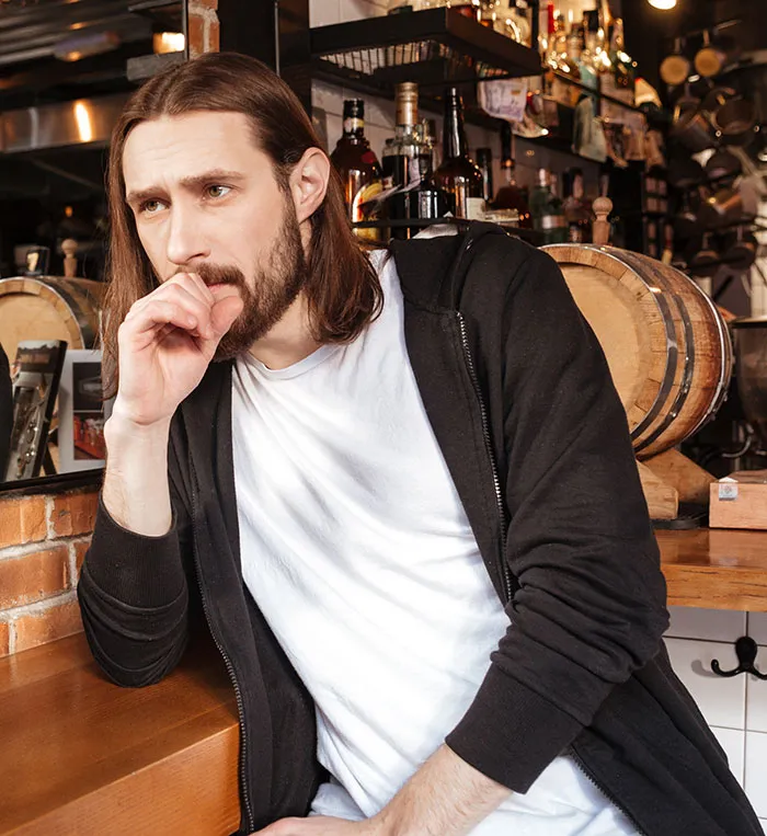 Young man in casual clothes sitting thoughtfully in a bar, reflecting on catfish stories and online DMs.