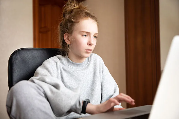 Young woman in casual clothes looking at laptop screen, reflecting on catfish stories and online DM experiences.