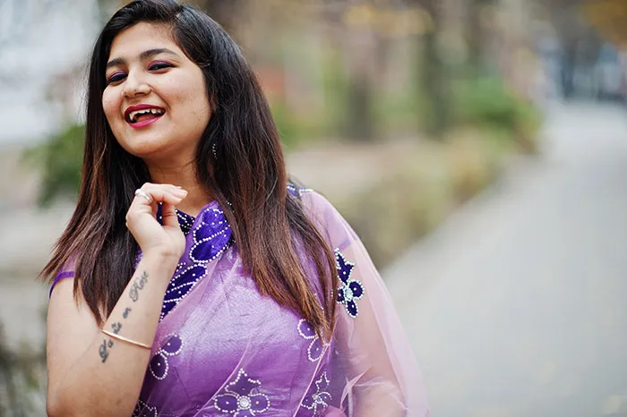 Young woman in a purple sari smiling outdoors, representing stories related to catfish encounters and online interactions.