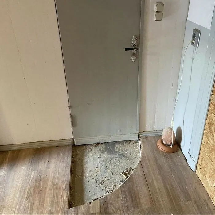 Fallo de construcción con suelo mal instalado frente a puerta gris, ejemplo divertido de fallos de construcción para reír y llorar.