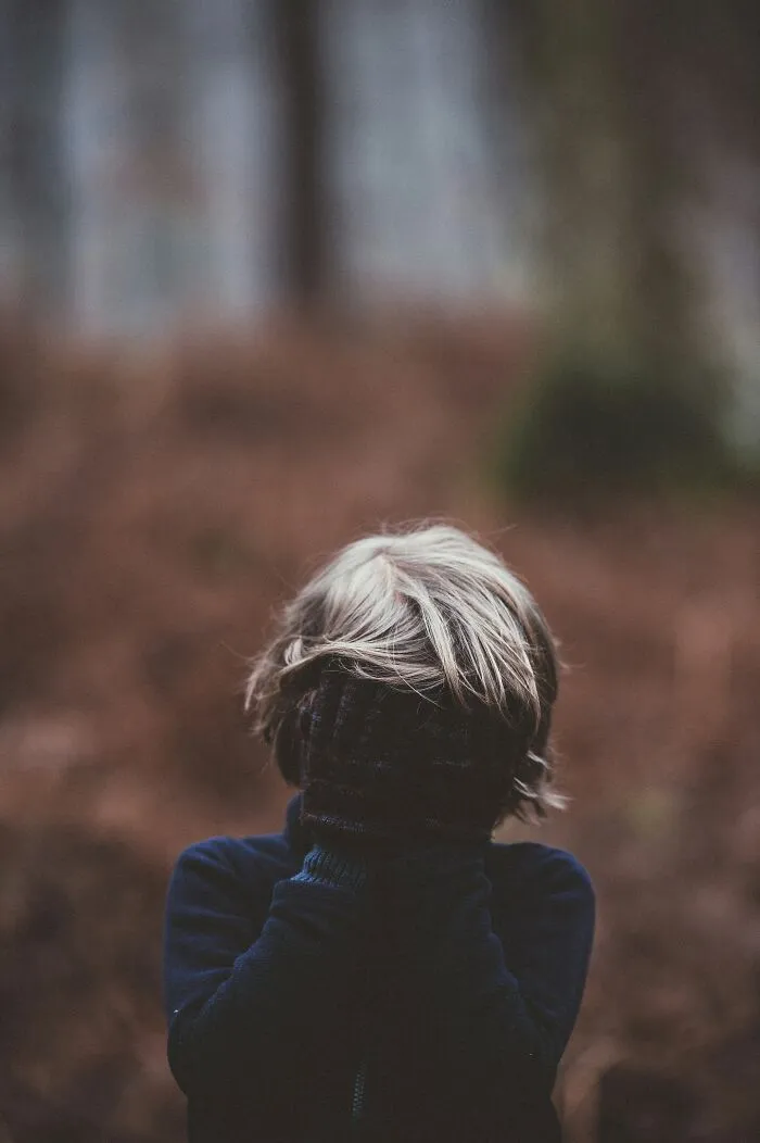 Child covering face in dark gloves and jacket outside, symbolizing stories from people who escaped death by pure luck.