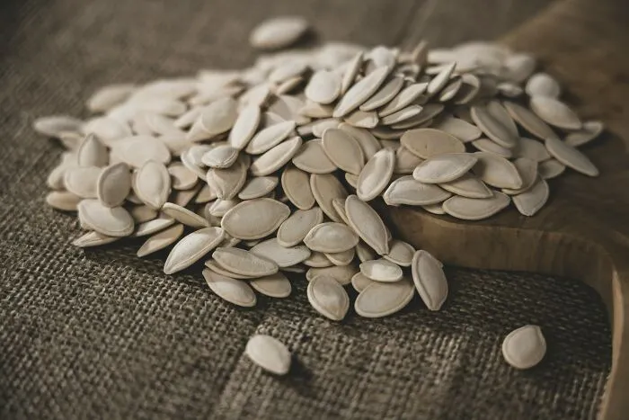 Close-up of pumpkin seeds scattered on a wooden board and textured fabric, symbolizing stories of escape by pure luck.