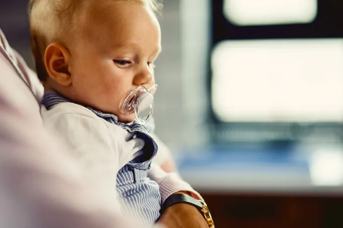 Baby with a pacifier being held by a medical professional, reflecting doctors and nurses experiences in healthcare settings.