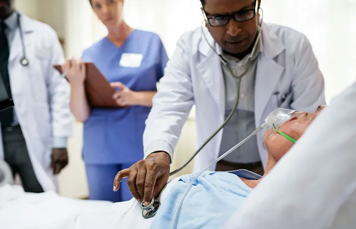 Healthcare workers examining a patient with oxygen mask in a hospital room, providing urgent medical care.