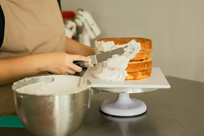 Person spreading frosting on a layered cake, illustrating a funny moment of people getting fired for silly mistakes.