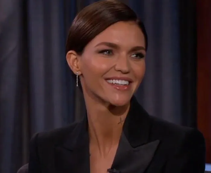 Smiling woman in black blazer shares insights on people who knew celebrities before fame in a studio interview setting