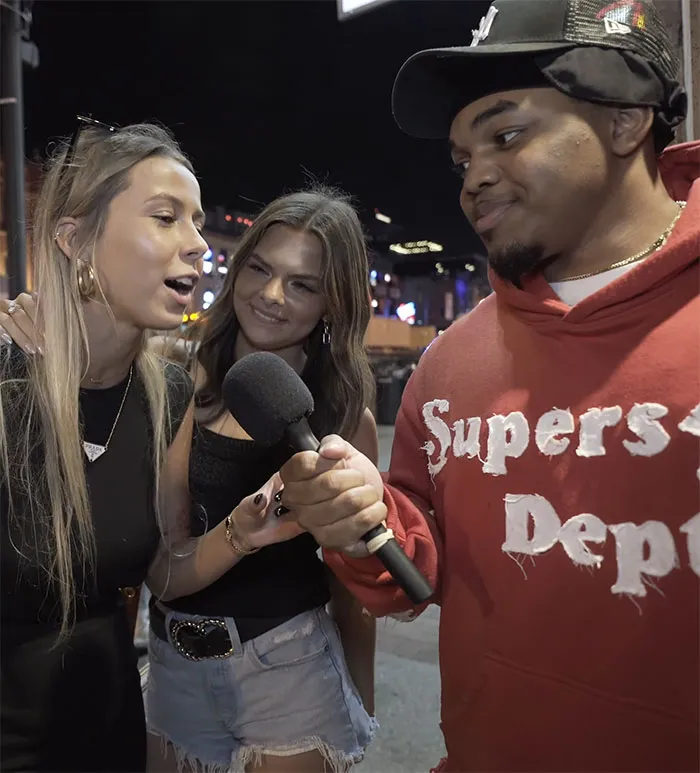 Two women and a man holding a microphone outdoors at night, discussing stories of people who ruined their lives fast.