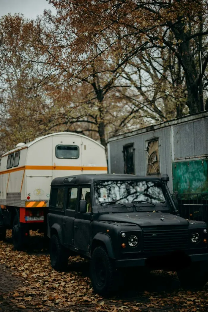 Black off-road vehicle parked near trailer and aging building in autumn forest, illustrating how dumb mistakes lead to consequences.