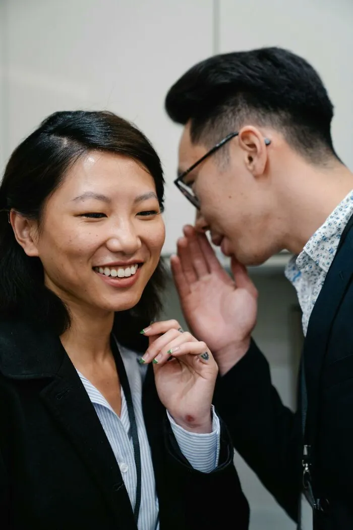 Two people whispering closely, illustrating the concept of the villain in someone else’s story and ruined life.