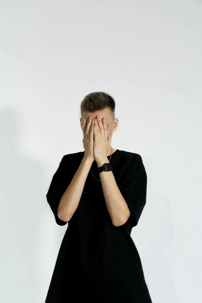 Young person covering face with hands, representing the villain in someone else’s story and ruined life concept.