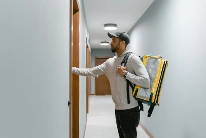 Man with delivery bag knocking on a door down a hallway, evoking themes of real-life hexes and odd curses.