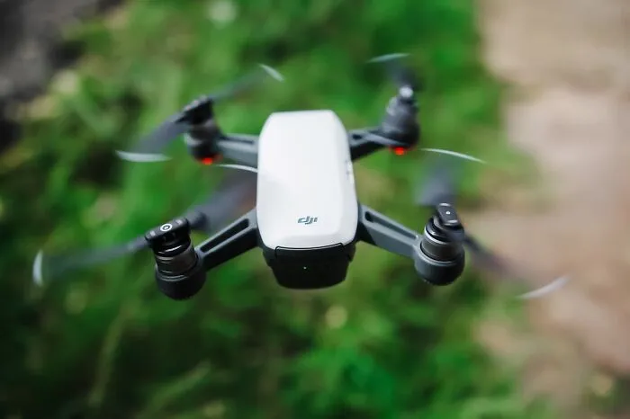 Small white DJI drone flying outdoors with blurred green and brown natural background, illustrating technology use and accidents.