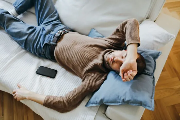 Man lying on couch looking frustrated and tired, phone beside him, illustrating moments people got fired due to dumb mistakes.