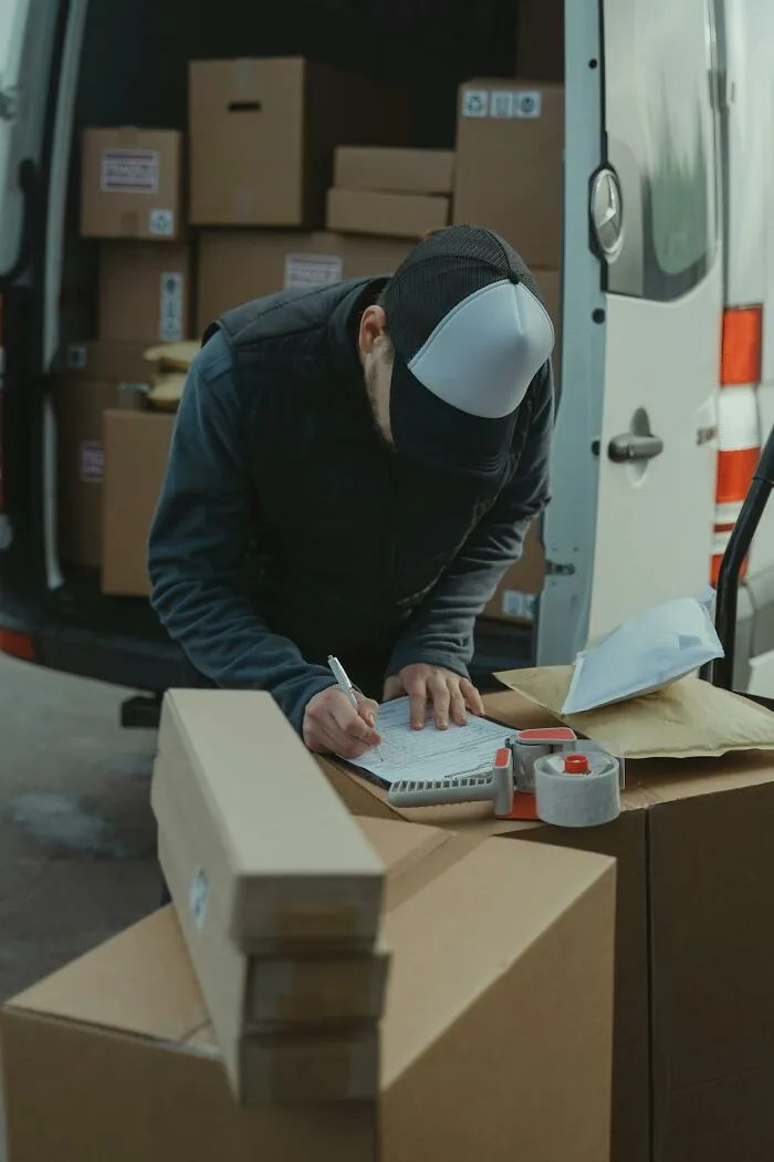 Delivery worker checking packages and signing documents amid stacked boxes, illustrating people who were the villain in stories.