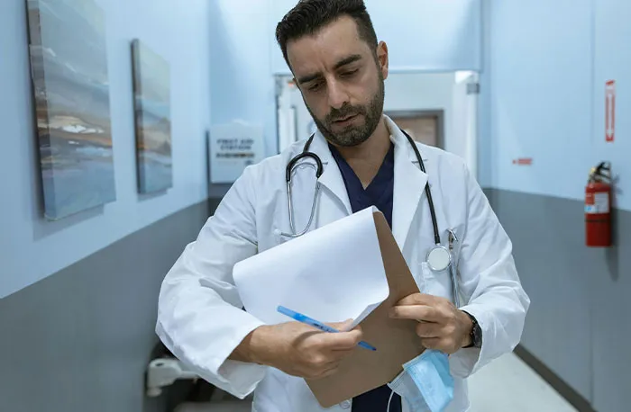 Doctor in white coat reviewing patient notes with stethoscope in hospital hallway discussing accurate diagnoses.