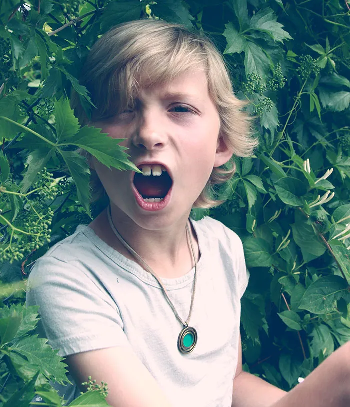 Young boy making a scared face among dense green leaves, evoking scary real-life stories with a shudder.