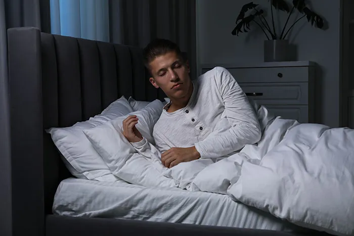 Young man in white pajamas lying awake in bed at night, looking scared, illustrating scary real-life stories.