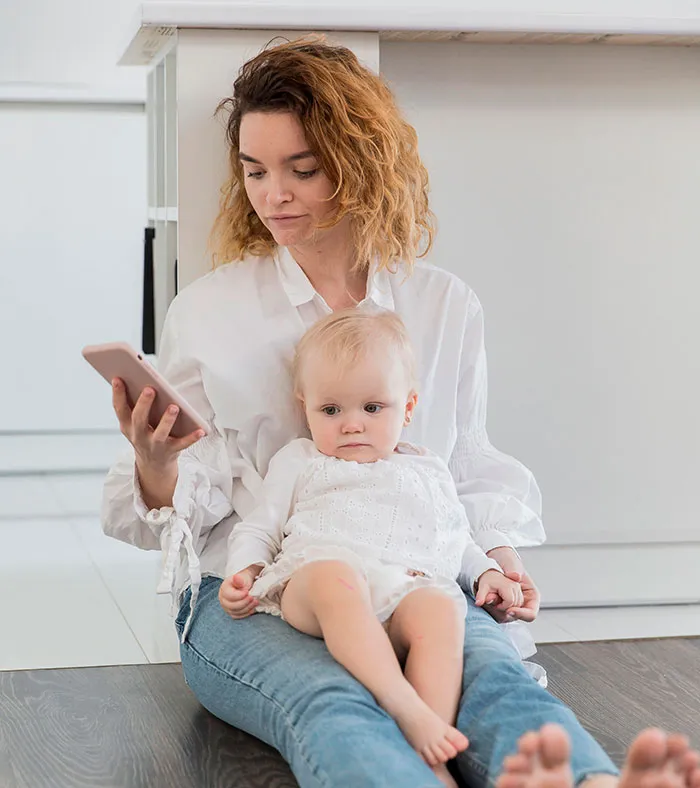 Woman holding baby and looking at phone, capturing a moment related to scary real-life stories and family emotions.