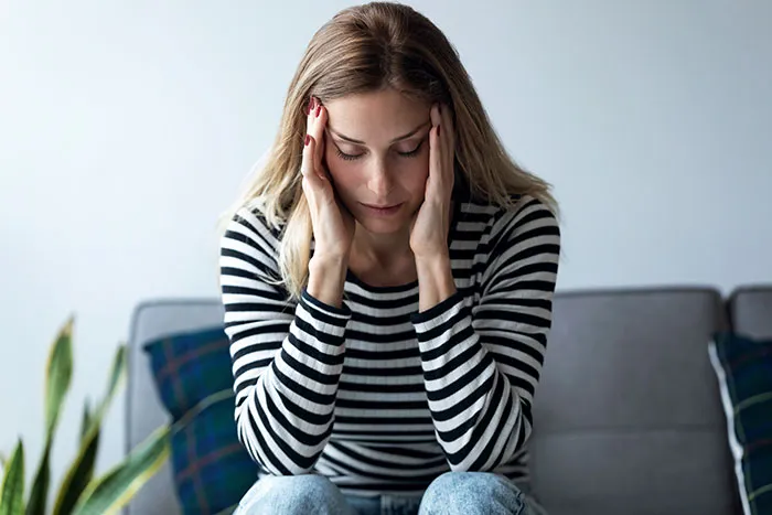 Woman in striped shirt sitting on couch, holding her head in hands, reflecting on scary real-life stories.