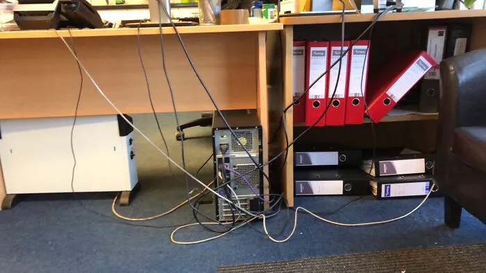 Tangled cables connected to a desktop computer under a desk, showing poor handling of electronics and wiring.