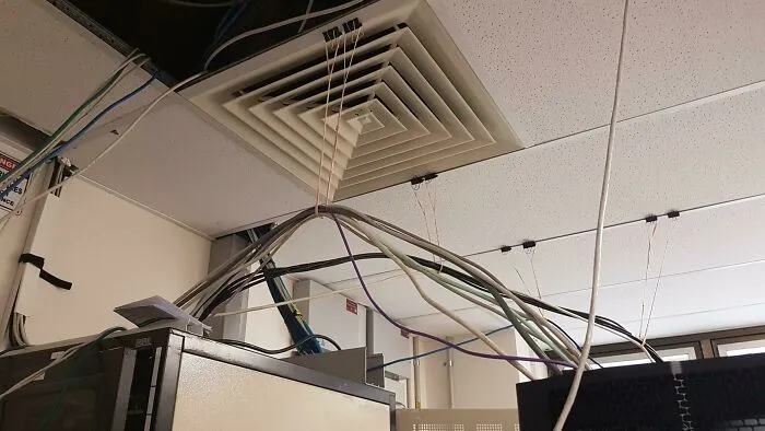 Tangled and unsupported cables hanging from ceiling in an office server room, showing poor handling of electronics.