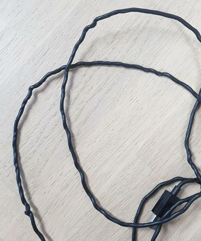 Twisted and damaged black electronic cable lying on a wooden surface, illustrating improper handling of electronics.